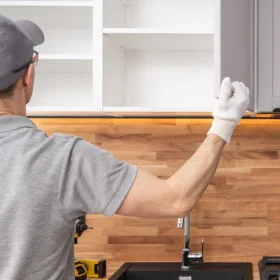 a person in a grey shirt and white gloves is working on a kitchen counter.